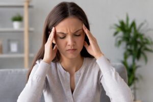 Mujer con dolor de cabeza sujetándose las sienes mientras presenta síntomas de cefalea en un ambiente interior.
